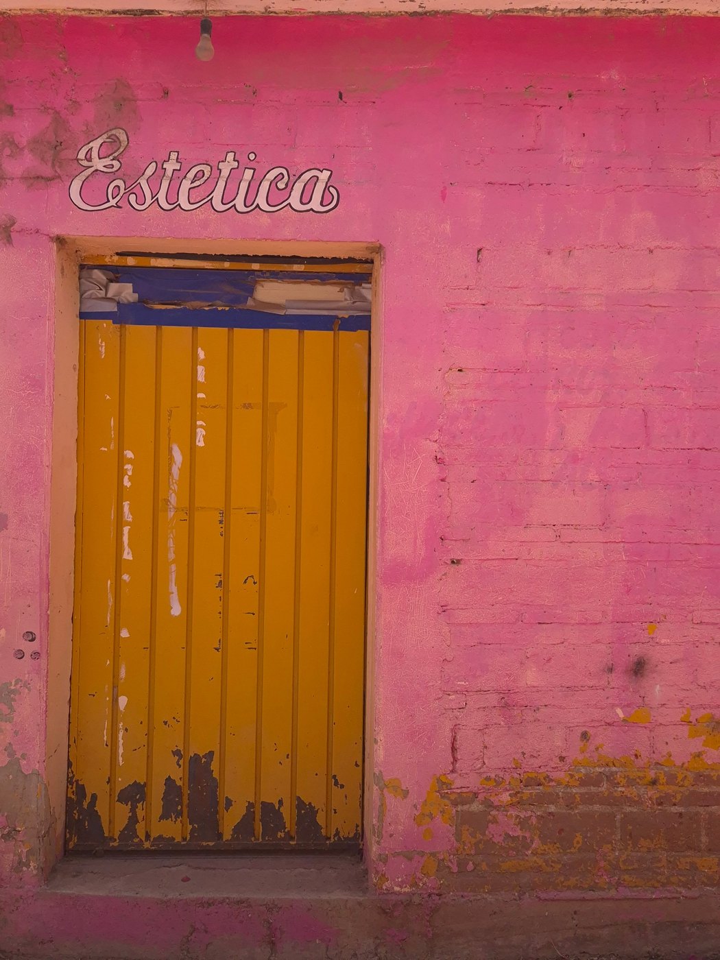 Pink wall with a yellow door and the word Estética