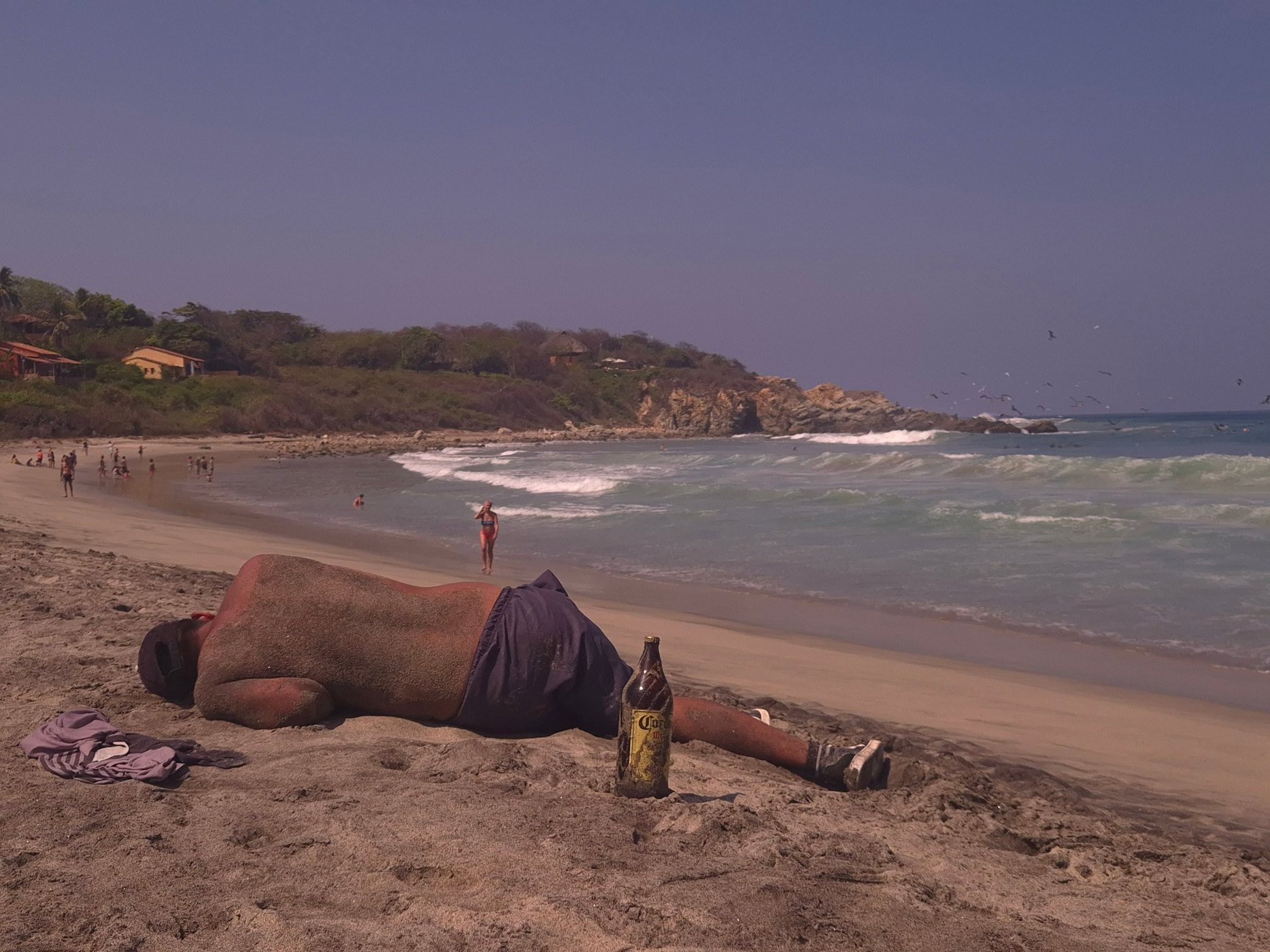 Man asleep on a beach beside a beer bottle