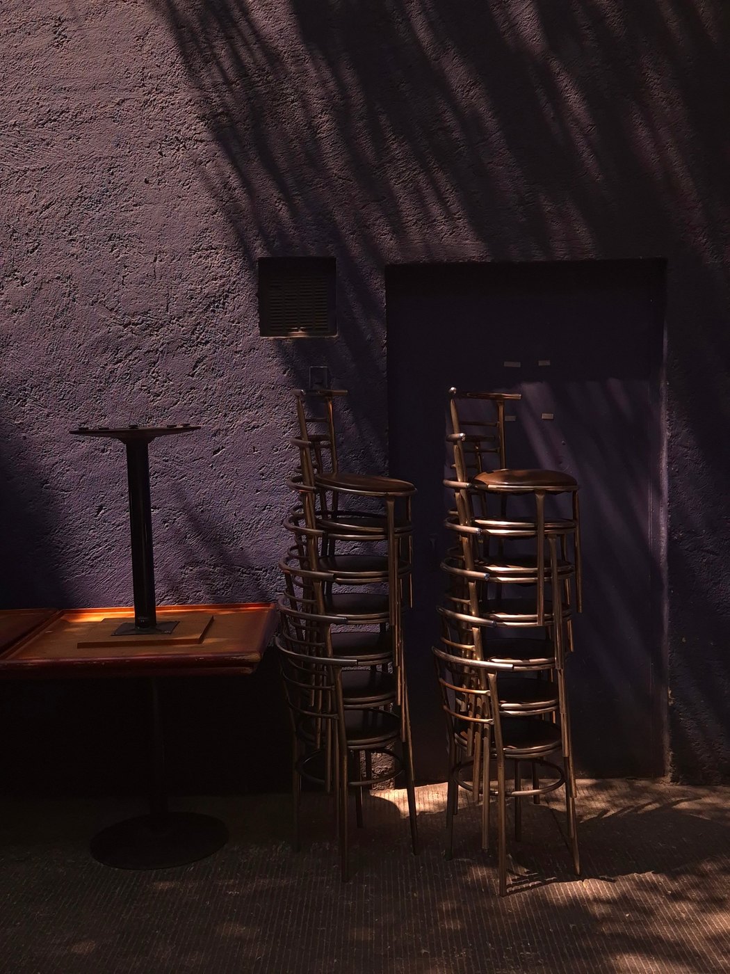 Stacked chairs against a violet wall with palm shadows