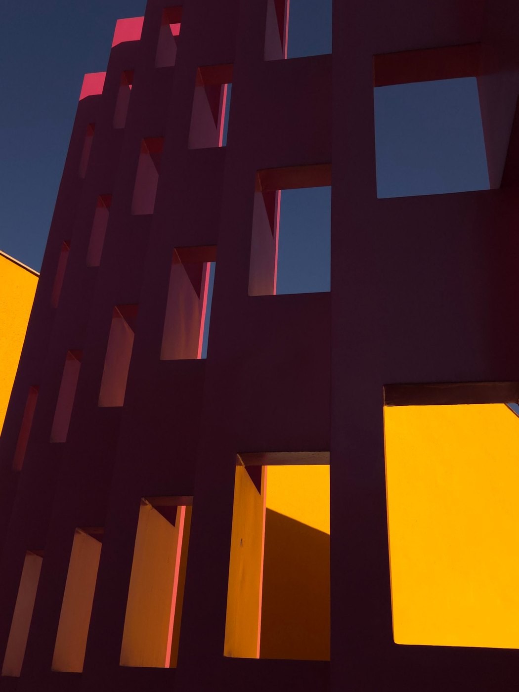 Deep pink facade with yellow light through square openings