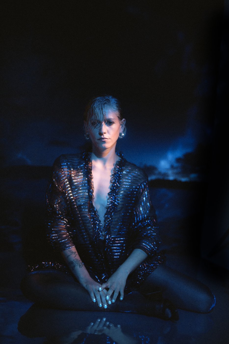 Seated portrait in a sheer sequined jacket, reflected on water