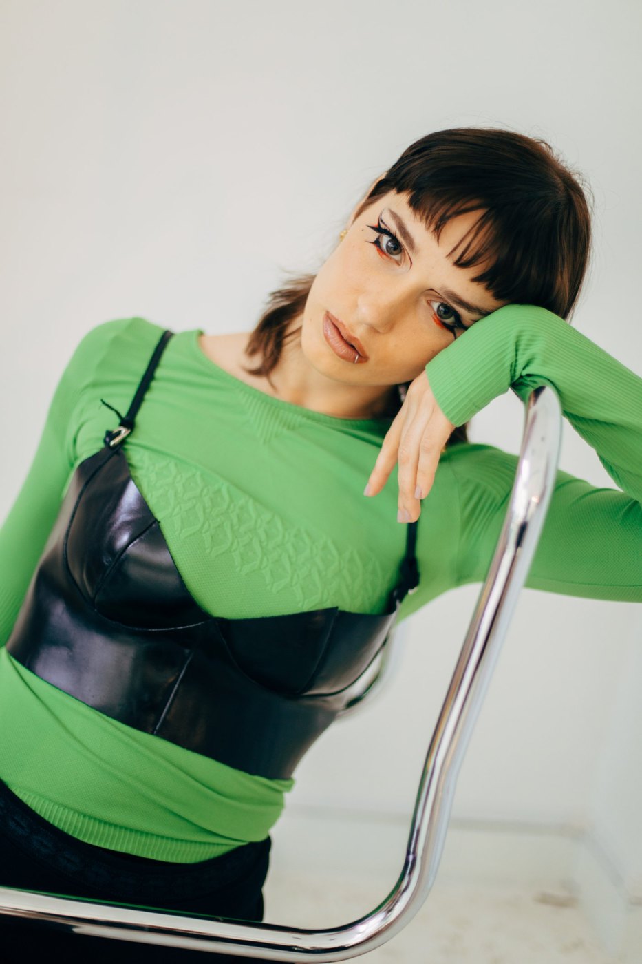 Portrait in green knit and black leather bustier on a chrome chair